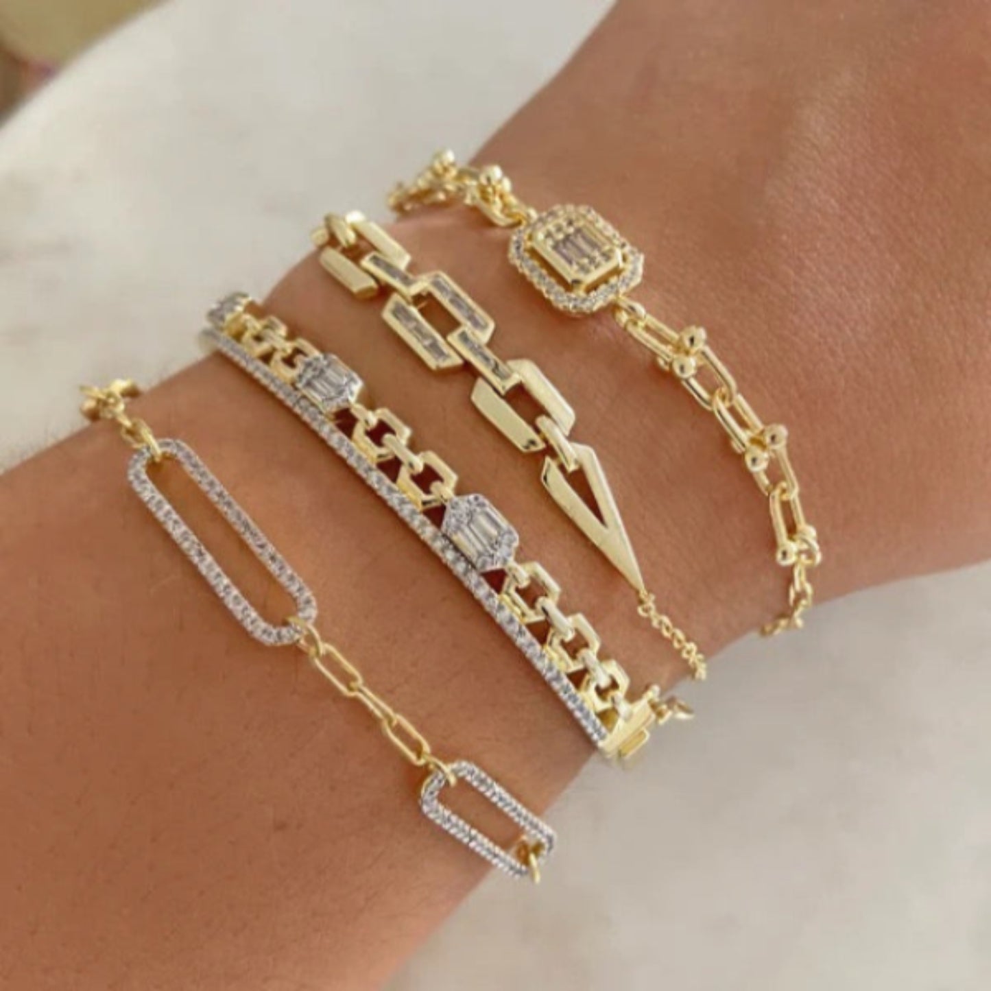 stack of gold link bracelets with geometric and diamond-accent designs on a wrist.