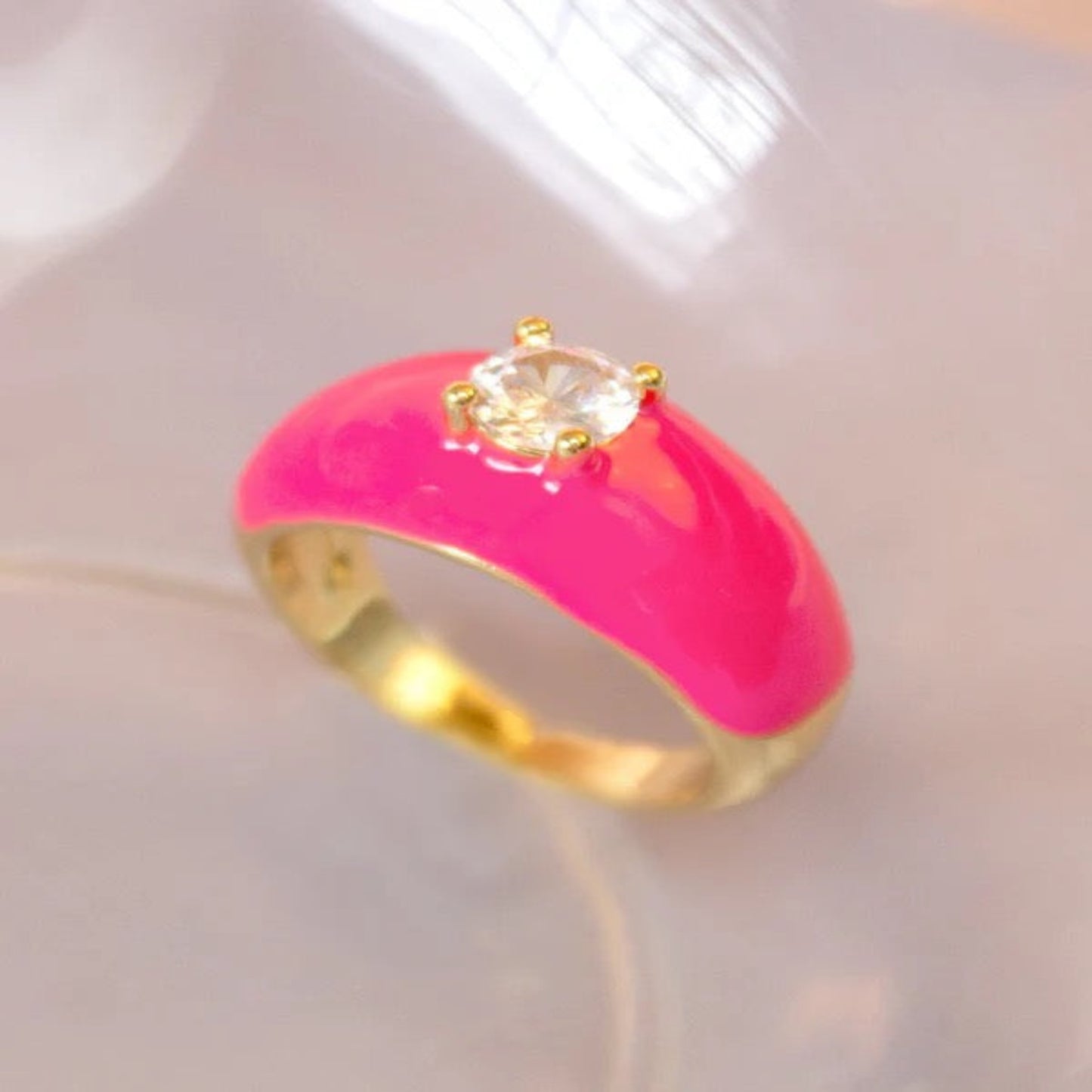 Gold ring with bright pink enamel and clear crystal on a soft background.