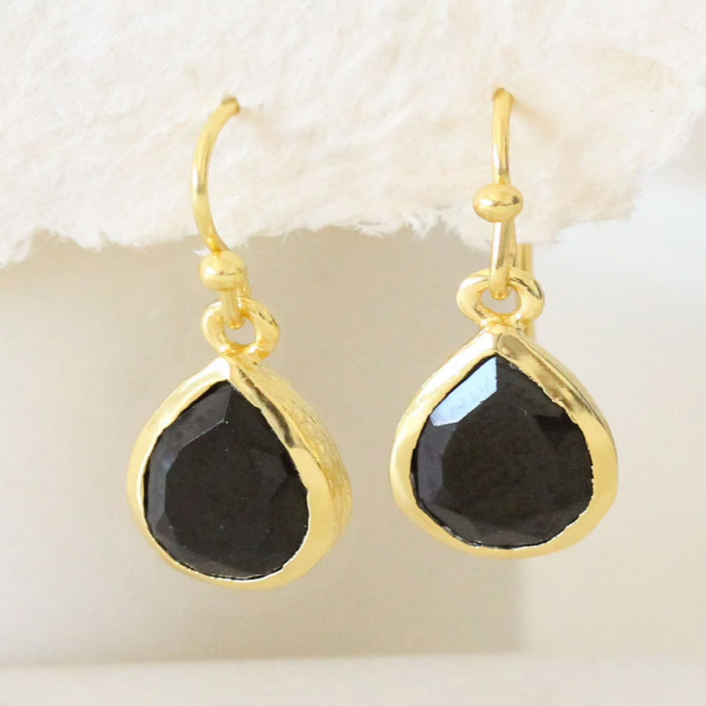 Gold teardrop earrings with faceted black onyx stones on a white background