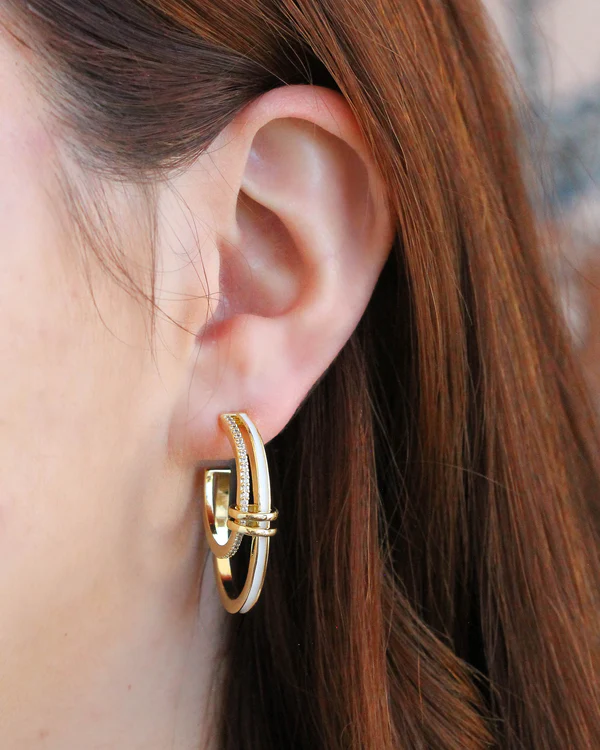 Close-up of a person wearing gold white enamel stud hoop earrings with blurred background