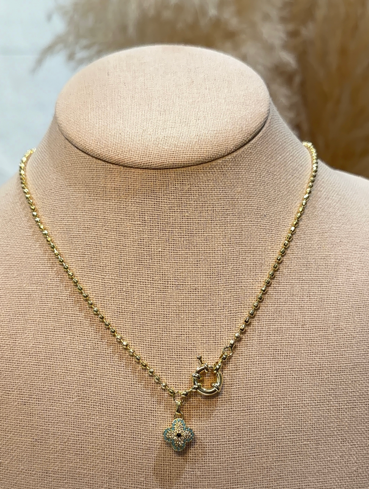 Gold necklace with a pendant on a mannequin bust.