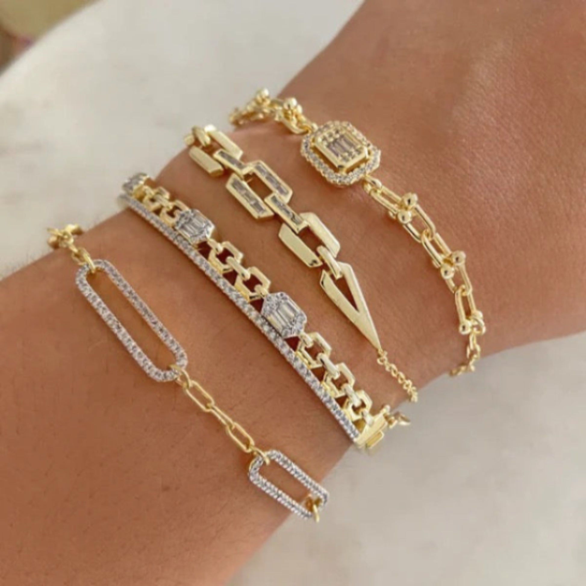 stack of gold link bracelets with geometric and diamond-accent designs on a wrist.