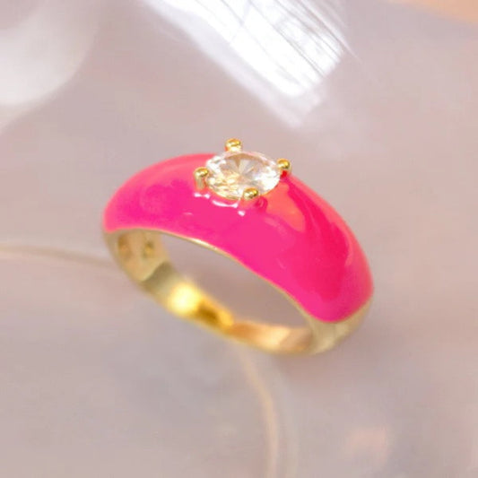 Gold ring with bright pink enamel and clear crystal on a soft background.