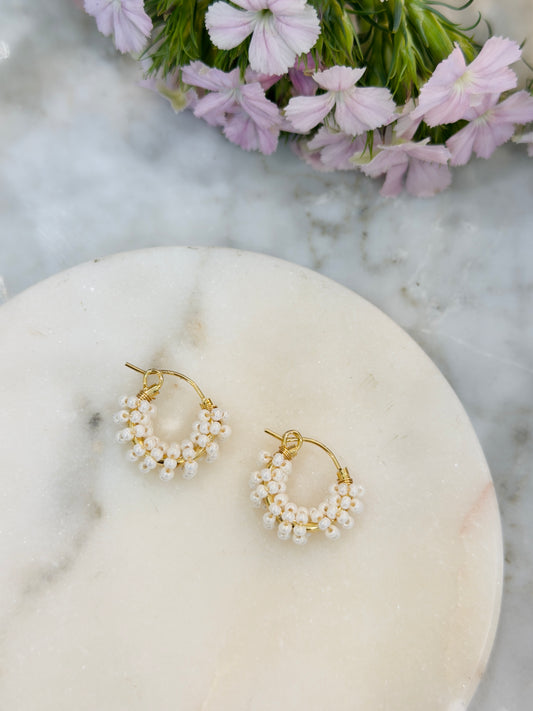 Gold hoop earrings with pearls on a marble surface with flowers in the background