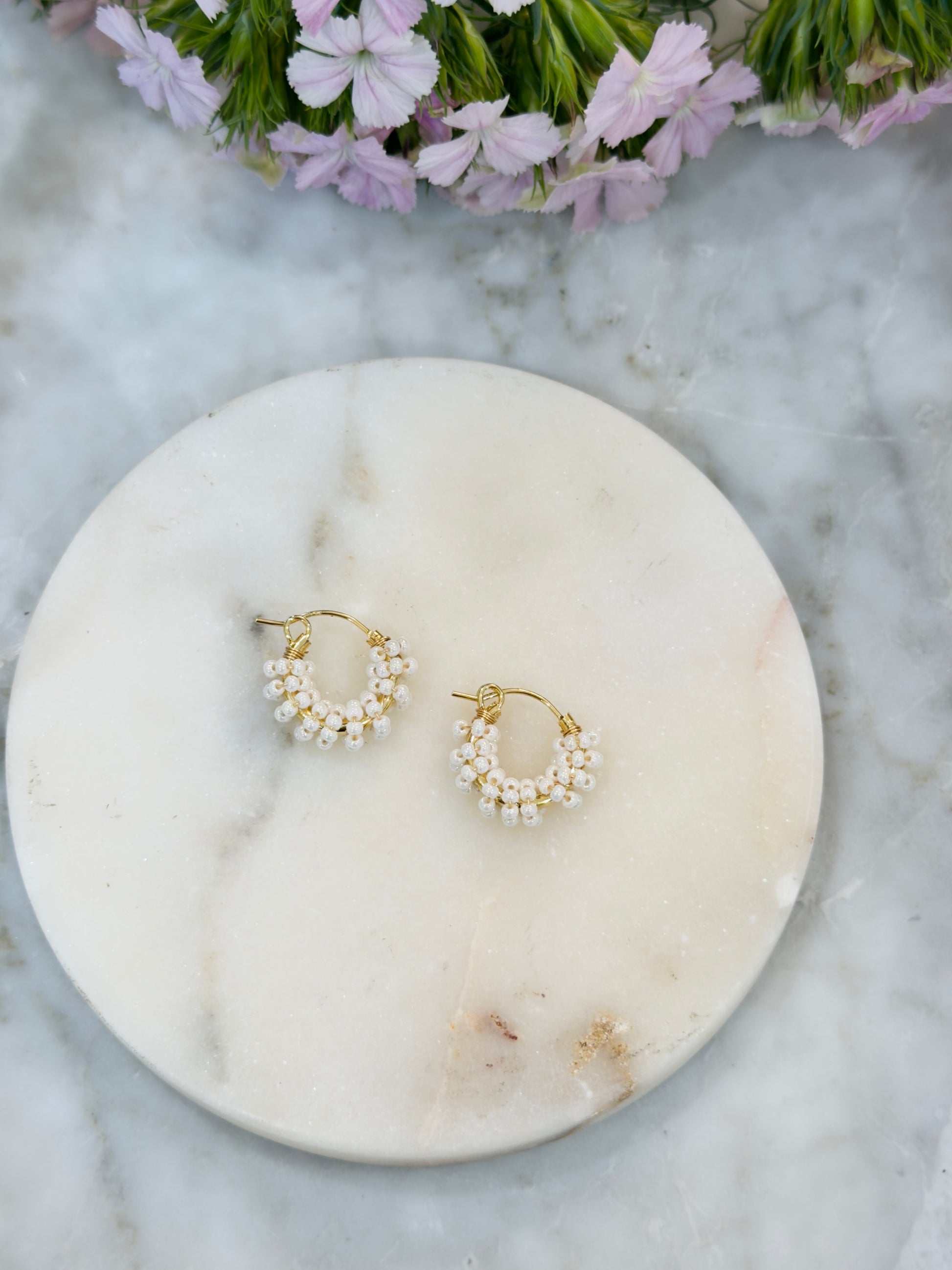Gold hoop earrings with pearls on a marble surface, surrounded by greenery.