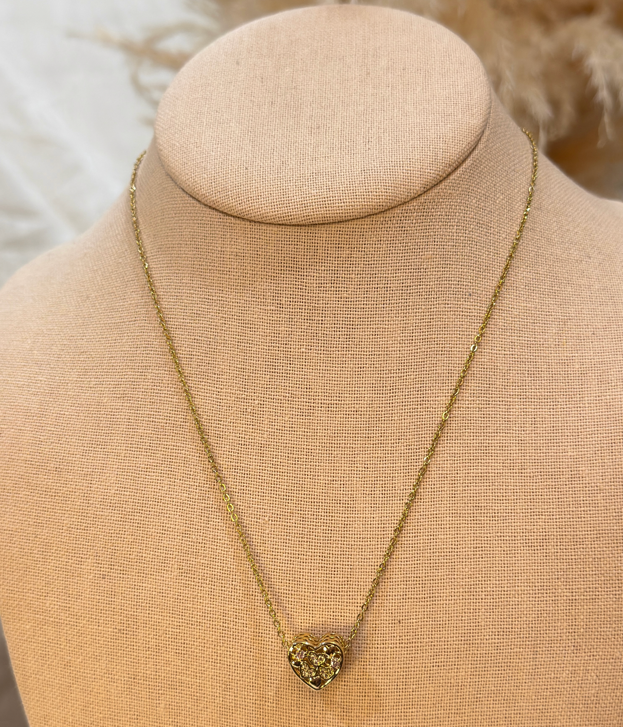 Gold necklace with a heart-shaped pendant on a beige mannequin bust.