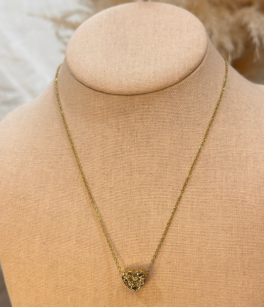 Gold necklace with a heart-shaped pendant on a beige mannequin bust.