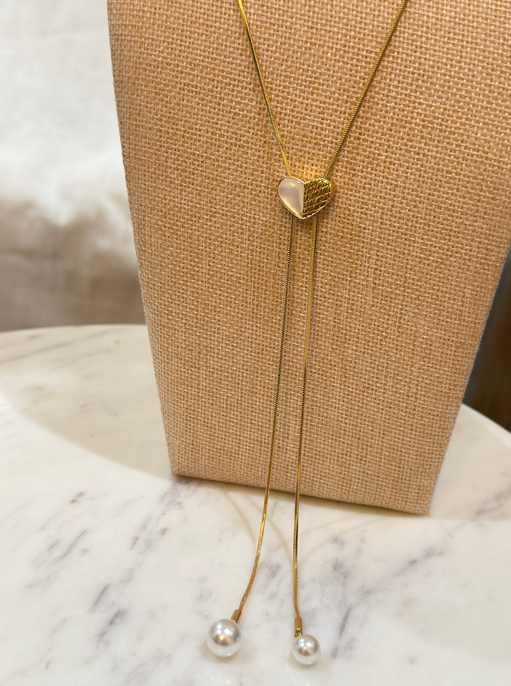 Gold necklace with heart pendant on a marble surface