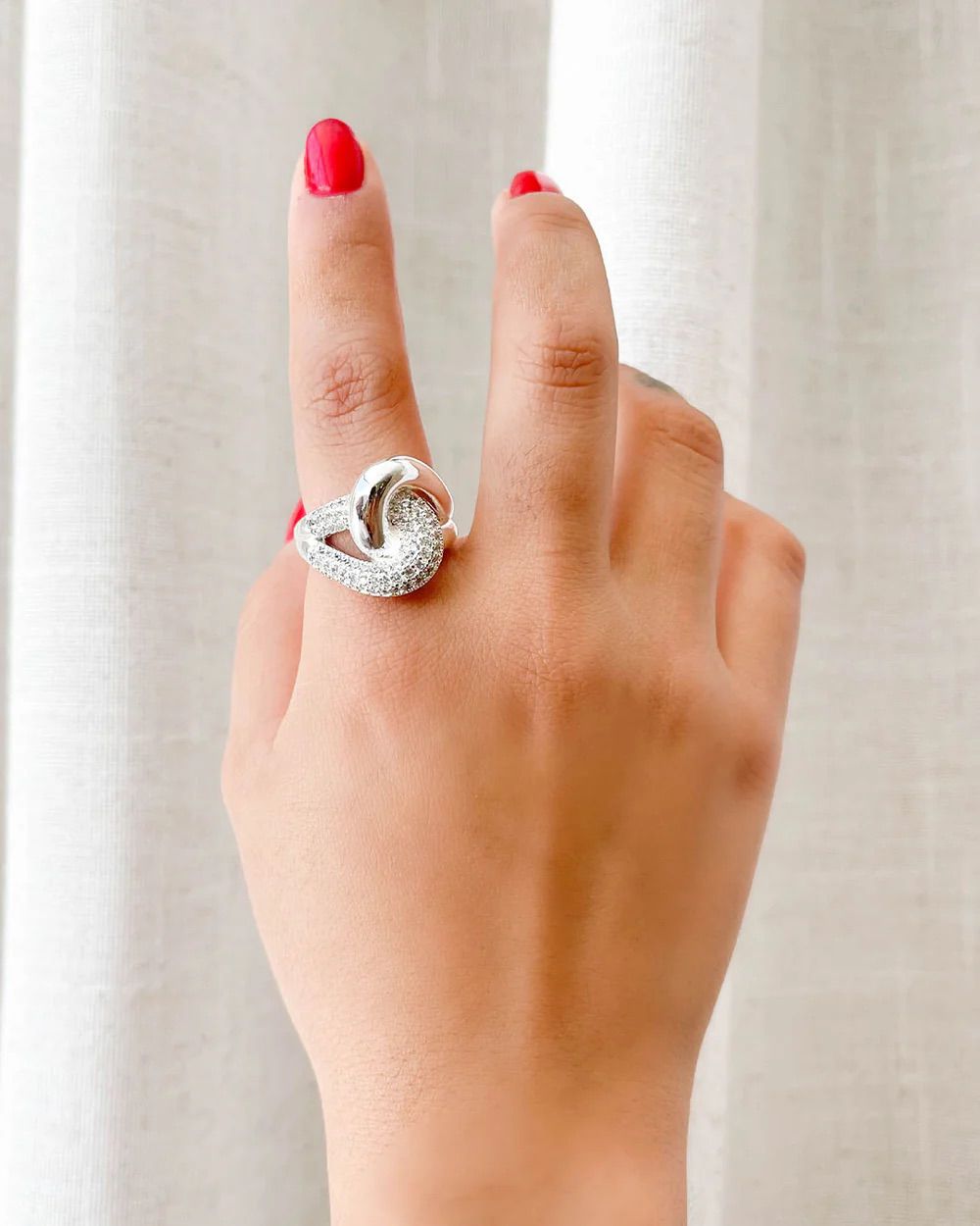 Hand wearing a silver ring with a diamond on a neutral background, statement ring for womens, womens ring fashion, ring statement piece, zirconia rings, thick silver band ring incrusted with zirconia