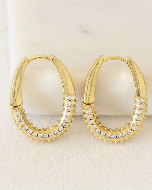 Gold hoop earrings with embedded zircon stones on a light background